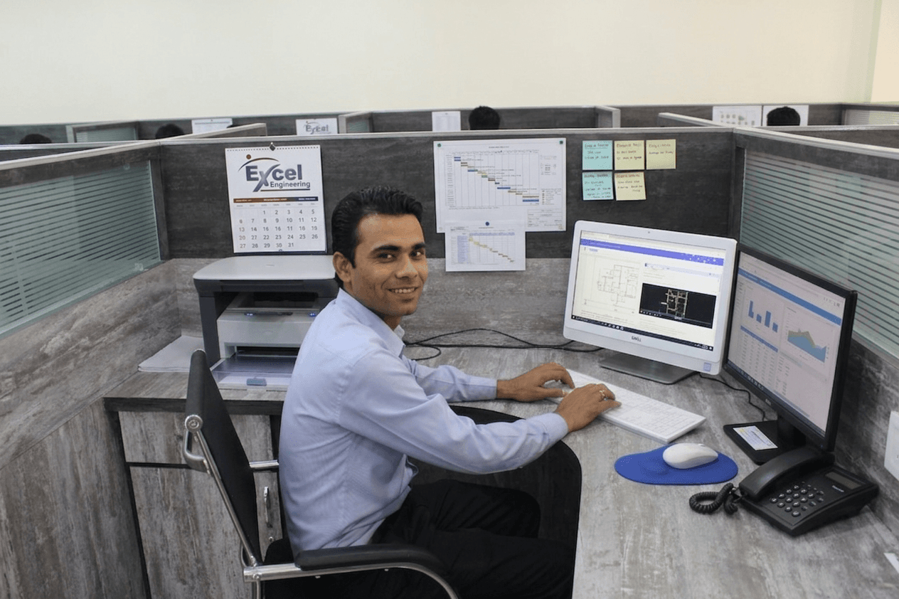 Engineer smiling at CAD workstation with dual monitors showing engineering drawings and dashboards