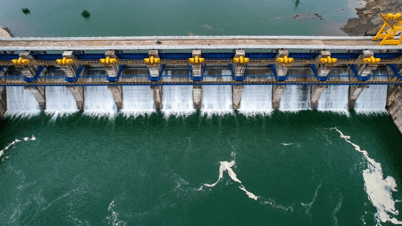 Top-down aerial of completed barrage with yellow hoists on blue steel frames, water cascading all bays